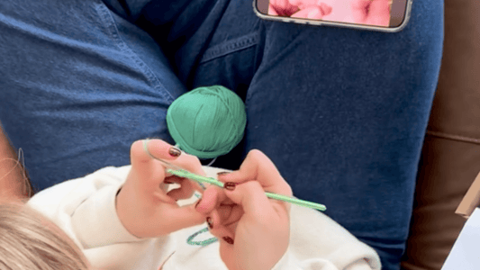 Girl learning to crochet watching video tutorial and following pattern